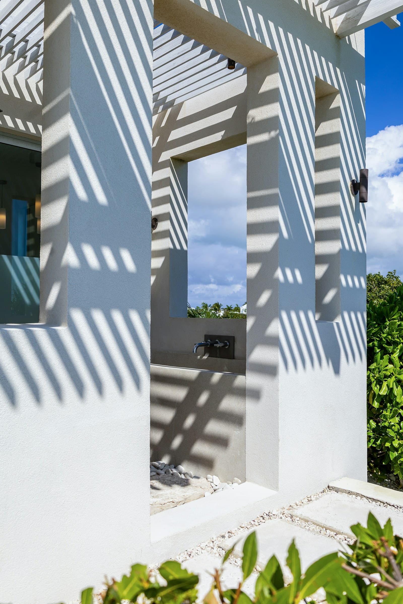 Outdoor shower with white pillars beneath a slatted roof casting striped shadows