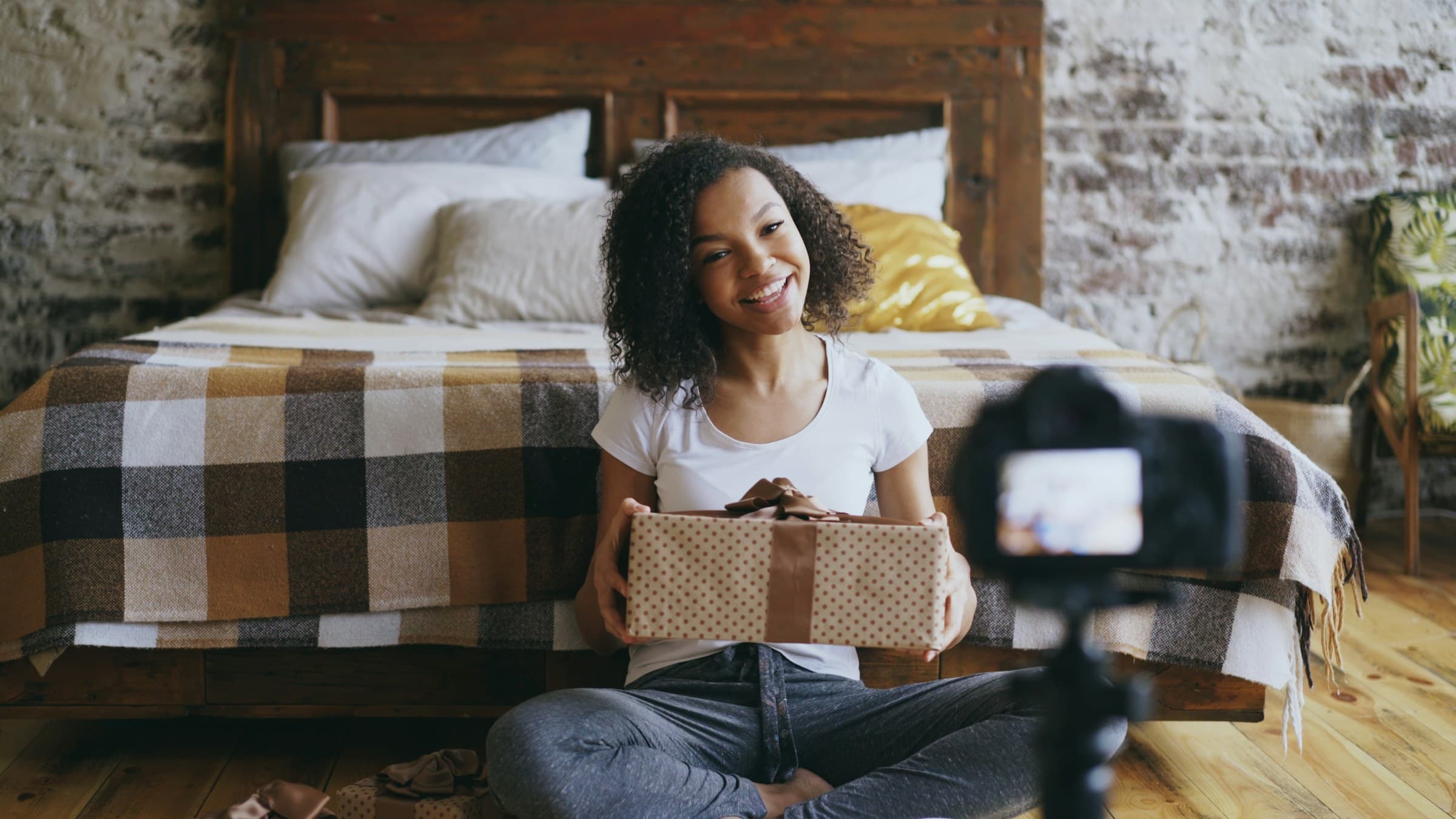 A creator presents a wrapped product to her camera while recording a review at home